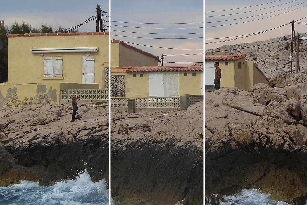 Kate Carr - Fabulations, two people stood on rocky shoreline with yellow houses behind, image split vertically into three slightly off-set sections