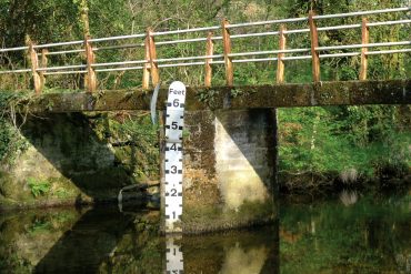 Simon Scott - Floodlines, bridge over water with a water height measuring stick