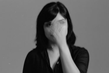 Sarah Davachi - All My Circles Run, black and white photo of artist waving her hand in front of her face