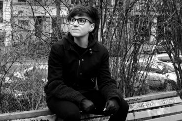 Julia Reidy - Beholder, black and white photo of the artist sat on a bench in a park.