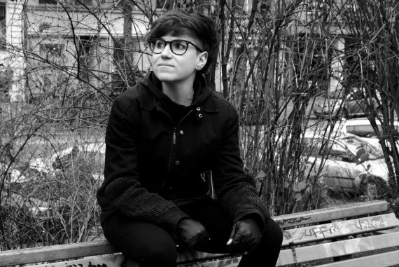 Julia Reidy - Beholder, black and white photo of the artist sat on a bench in a park.