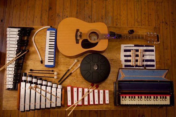 Ensemble 0 - plays eight compositions, top-down view of a guitar, glockenspiels, harmonium, metallophone, and other instruments laid on a table.